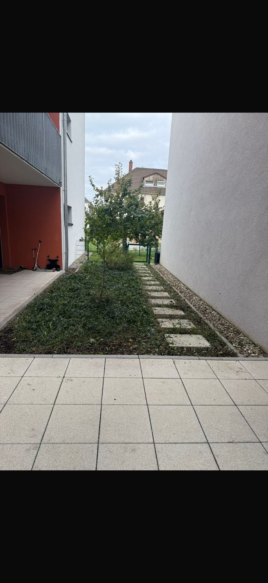 Gepflasterter Innenhof zwischen weißen Gebäuden mit sauberen Heckenstreifen und Trittsteinen nach der Neuanlage