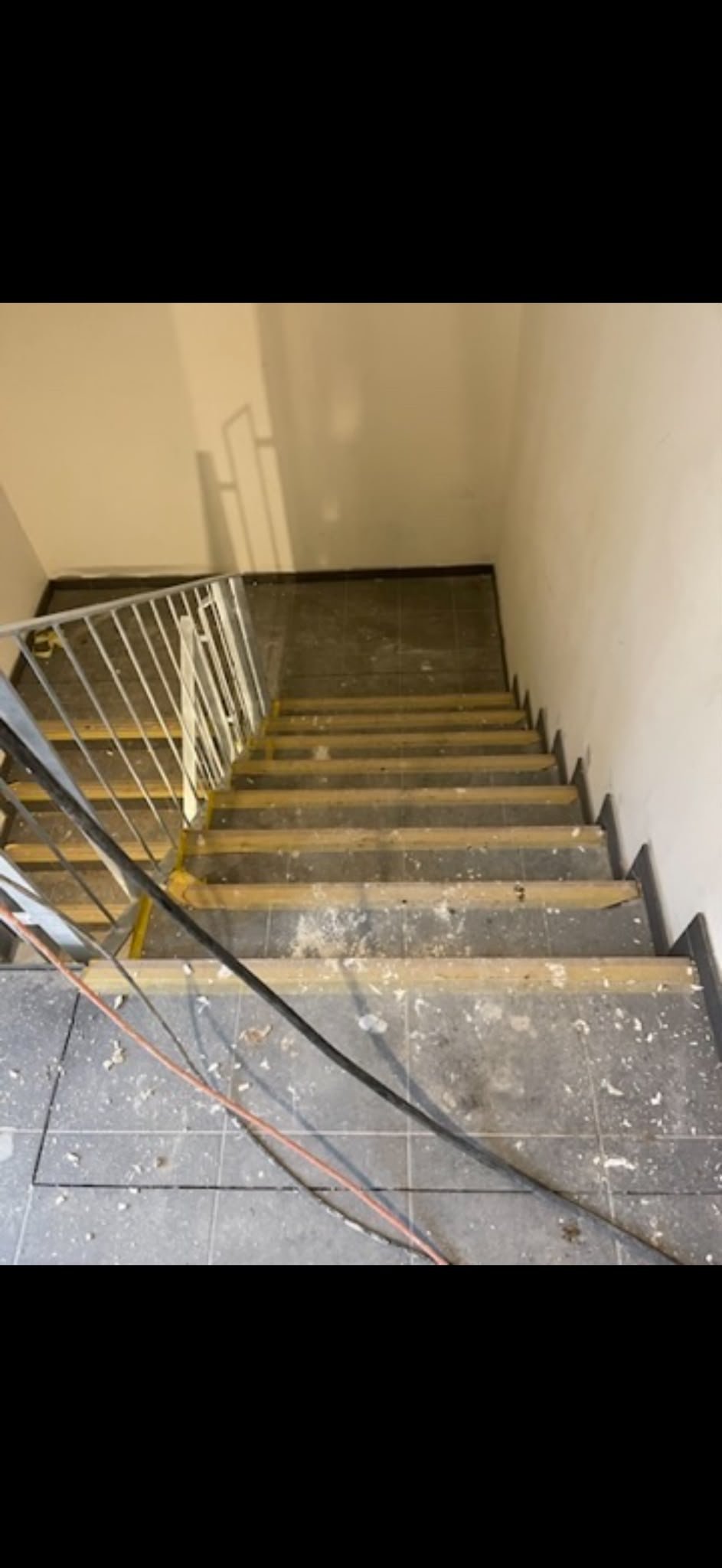 Innentreppe mit weißem Metallgeländer und Holzstufen während der Bauphase, offene Kabel verlaufen entlang der Wand