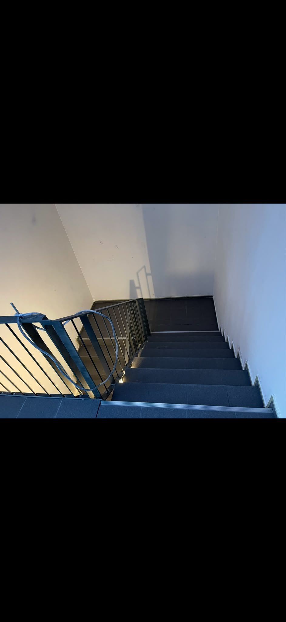Fertiggestellte Treppe mit dunklen Stufen und Metallgeländer, die sich vor hellen weißen Wänden nach oben zieht