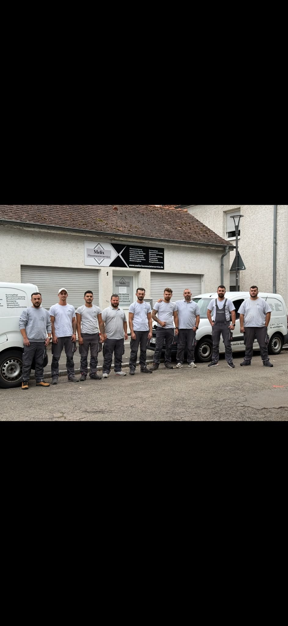 Team of workers in matching light blue shirts standing in a line in front of a building and white service vans