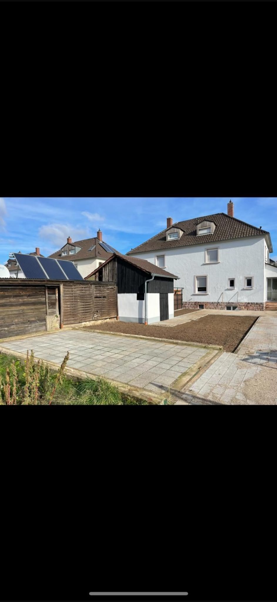 Gepflegter Garten mit weißem Haus, Holzschuppen und gepflasterter Terrasse unter klarem Himmel