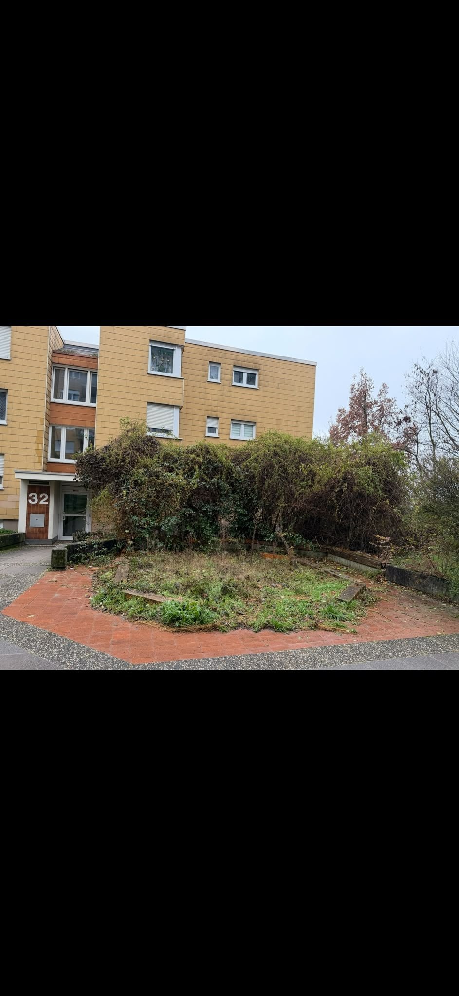 Dreigeschossiges Wohngebäude mit gepflegtem Vorgarten, geschnittenen Hecken und sauberem Backsteinweg